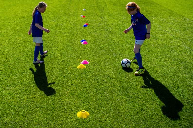 To jenter, 1 ball og flere kjegler.